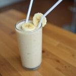 Batido de banana natural servido em um copo, decorado com uma fatia de banana.