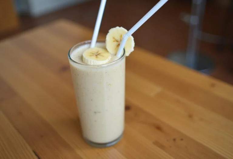 Batido de banana natural servido em um copo, decorado com uma fatia de banana.