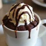 Bolo de caneca de chocolate finalizado, com sorvete e calda de chocolate, perfeito para servir.