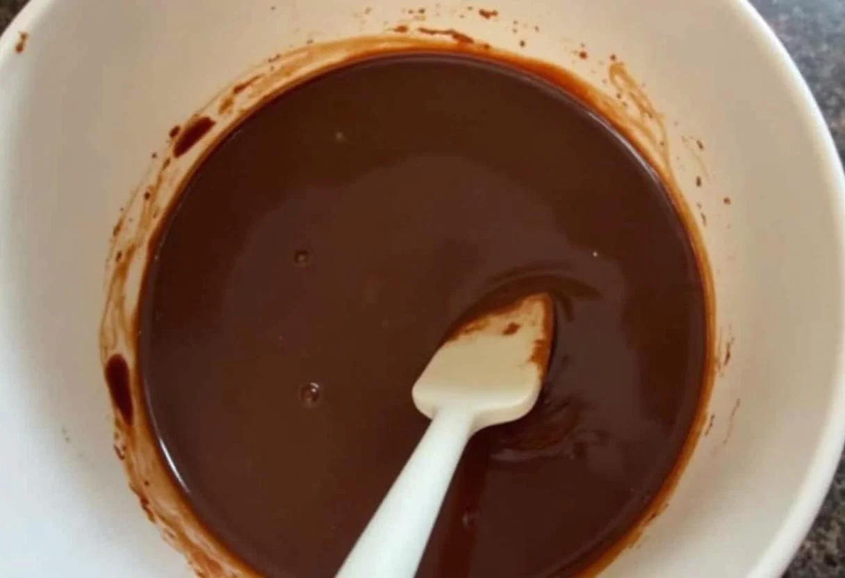 Chocolate derretido liso sendo mexido para a preparação de Conguitos de Chocolate.