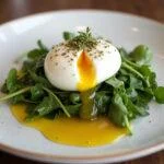 Perfectly plated gema de ovo poché with fresh greens and olive oil, ideal for a sophisticated brunch.