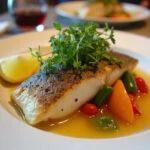 Prato final de peixe ruivo em papillote, decorado com ervas e legumes frescos.